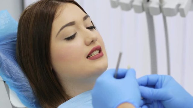 Color matching to make veneers using samples, choosing shade for young brunette woman patient teeth at dental clinic. Dentist appointment.