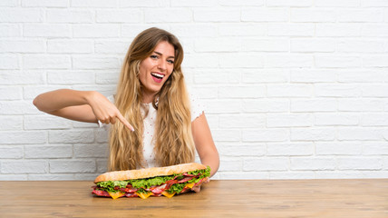 Happy Young blonde woman holding a big sandwich
