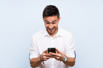 Handsome young man over isolated blue background surprised and sending a message