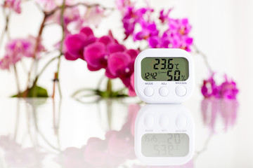 White electronic hygrometer on white table with orchids on the background