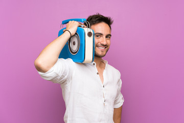 Fototapeta premium Handsome young man over purple background holding a radio