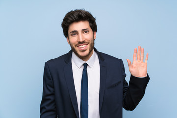 Businessman over isolated blue wall saluting with hand with happy expression