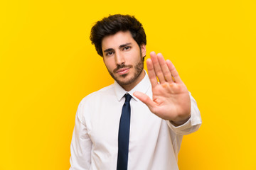 Businessman on isolated yellow background making stop gesture with her hand