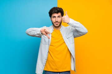 Handsome over isolated colorful background making good-bad sign. Undecided between yes or not