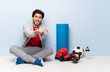 Sport man sitting on the floor holding copyspace imaginary on the palm to insert an ad