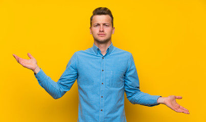 Blonde man over isolated yellow wall unhappy for not understand something