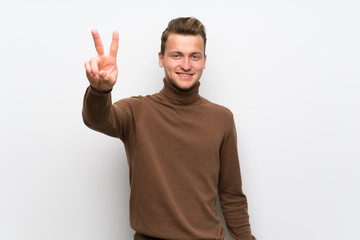 Blonde man over isolated white wall smiling and showing victory sign