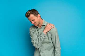 Blonde man over isolated blue wall suffering from pain in shoulder for having made an effort