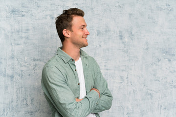 Blonde handsome man with green shirt standing and looking to the side