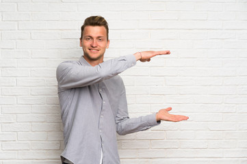 Blonde man over white brick wall holding copyspace to insert an ad