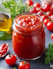 Traditional tomato sauce in a glass jar with fresh herbs, tomatoes and olive oil. Close up.