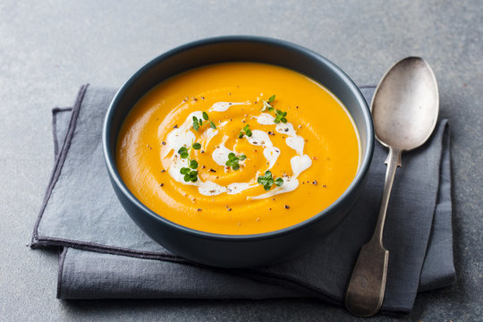 Pumpkin, carrot cream soup in a black bowl. Grey background.
