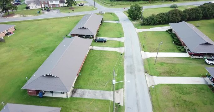 A drone or aerial shot of a section of a suburban residential neighborhood with houses, driveways, roads, lawns, trees and greeneries.