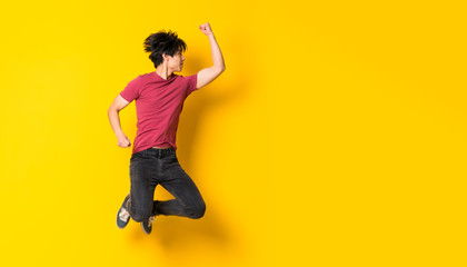 Asian man jumping over isolated yellow wall