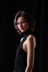 Fototapeta premium Young beautiful dark-haired girl in a black T-shirt on a dark background