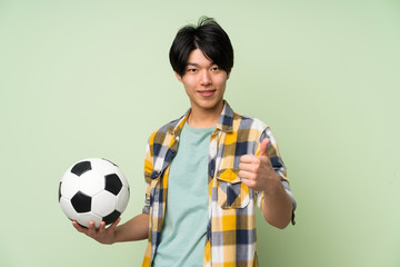 Asian man over isolated green wall holding a soccer ball