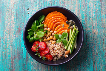 Healthy vegetarian salad. Roasted pumpkin, quinoa, tomatoes, green salad. Buddha bowl. Blue wooden background. Top view.