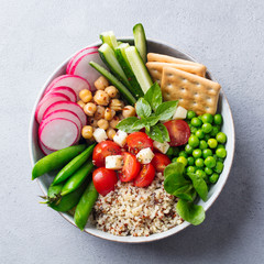 Healthy vegetarian salad. Buddha bowl. Quinoa, chickpea, tomatoes, pea, radish, cucumber, crackers. Grey stone background. Top view.