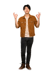 A full-length shot of a Asian man with brown jacket in zen pose over isolated white background