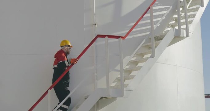 Young engineer walking up ladder of refinery tank for checking valves and safety systems