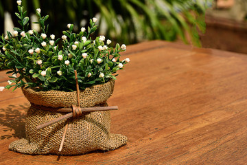 Flowers in a hemp sack pot with a rattan band on a brown wood table.