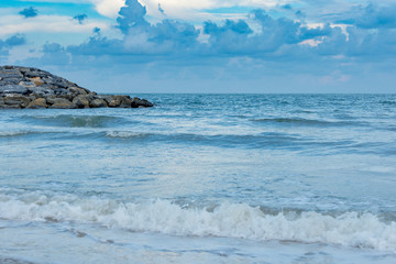 The blue sea creates waves by the white sea breeze blowing into the shore.