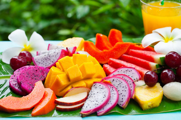 Tropical fruits assortment with fresh juice, palm leaf background. Close up.