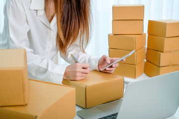 Beautiful young entrepreneur woman about an online business sitting working at home with a package box and taking note. Smiling and laughing happily.