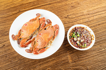 A dish of steamed three-pointed crab and sauce on a wooden table