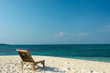Wooden chairs on the white sandy beach with little waves, blue and bright blue sky.
