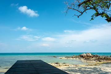 Wooden bridge for sitting on the beach resort Clear sea water with blue sky There is a small rock formation on the beach.
