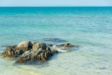Clear sea, white sand beach, rocks in the sea and blue sky