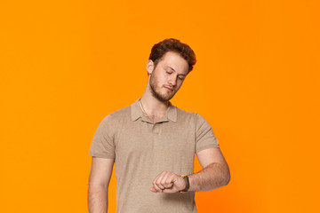 Studio shot of a bearded young man looking at the wristwatch.