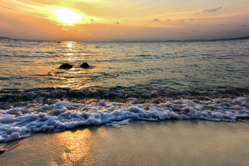 The background of the white sea waves strikes the rocky shore of the golden sand in the evening.