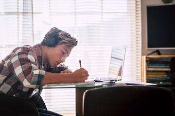 Close up of teenager with headphones staring at laptop doing his homework in silence - indoor focus guy
