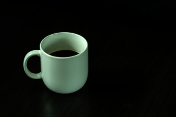 White coffee cup, black coffee on black background with light and shadow