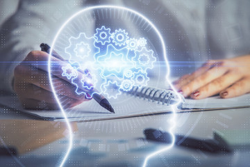 Double exposure of woman's writing hand on background with brain hologram. Concept of brainstorming.