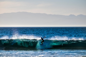 Obraz premium teenager surfing at the wave in tenerife playa de las americas - white wetsuits and beautiful and perfect wave