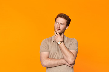 Young bearded confident man with hand raised on chin and looking aside.