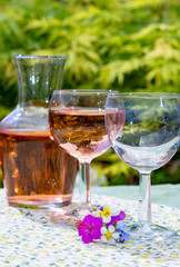 Wine carafe and glasses with cold rose wine and wild flowers in summer sunny day