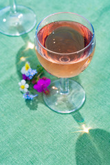 Glass with cold rose wine and wild flowers in summer sunny day