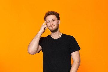 Studio shot of a bearded young man pointing a finger at the temple. Concept of a positive thinking.