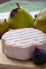Round piece of French cheese Fleur Rouge made from cow milk served as dessert with fresh figs and pears