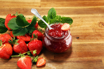 strawberry jam with fresh strawberries and mint. marmalade on spoon and jar on brown wood