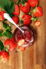 strawberry jam with fresh strawberries and mint. marmalade on spoon and jar on brown wood