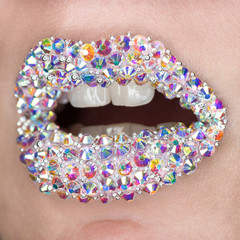 Beautiful closeup with female lips with white colorfull gemstones. Open mouth with white teeth. Make-up, lip art