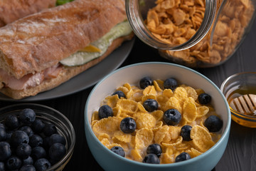 Food. Breakfast. Homemade delicious corn flakes with fruit and honey, baguette on black table on kitchen
