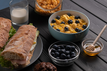Breakfast. Morning meal. Homemade food. Kitchen. Fresh sandwich, baguette, corn flakes with honey and berry. Black table