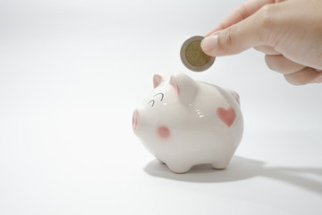 White piggy bank with a hand holding Thai baht coin ready to put in