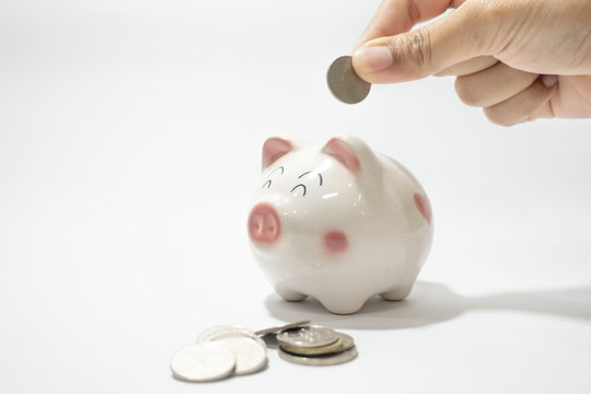 White piggy bank with a hand holding Thai baht coin ready to put in